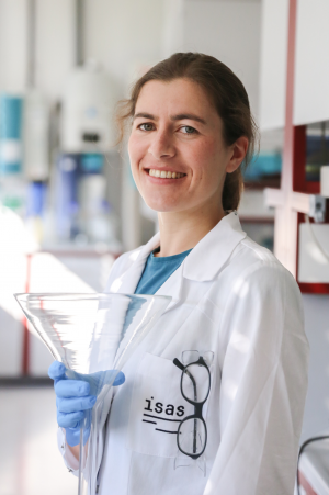 A Foto of Mona Ehlers in the laboratoy. She is wearing a lab coat and holding a glas funnel.