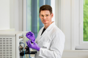 Daniel Foest steht im Labor und hält ein Papier mit einer Leberprobe, die er am Massenspektrometer untersucht.